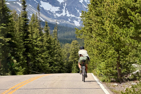 Someone riding their bicycle on a mountain road with peaks visible in the distance