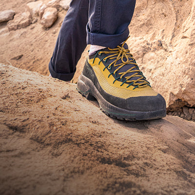 A closeup of a person in approach shoes hiking across rock