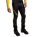 A person wears La Sportiva Stratos VI Racing Pants Men's in black and yellow with black buckled mountain boots, standing against a white background. Only the lower torso and legs are visible.
