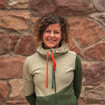 Woman wearing a green and beige quilted jacket with red drawstrings against a stone wall.