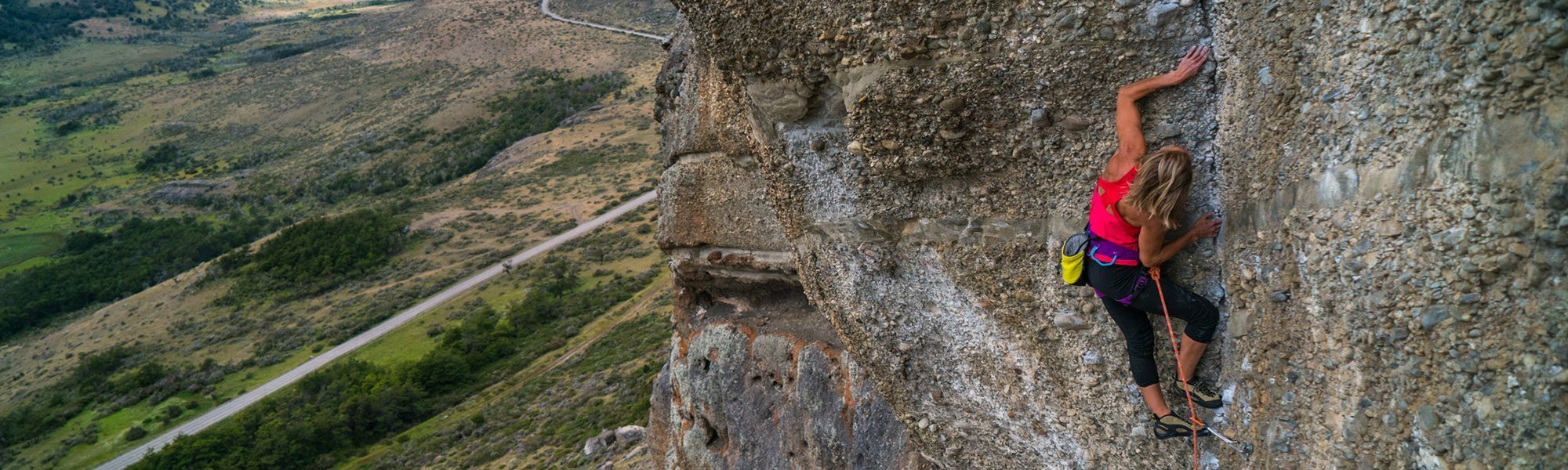 Person climbing a rocky cliff face with a scenic landscape in the background