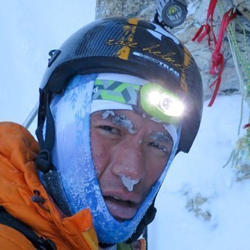 Person wearing a helmet and face cover with a headlamp in a snowy environment