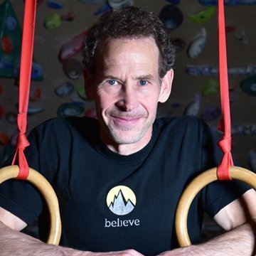 Man holding gymnastic rings with a climbing wall background