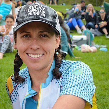 Woman wearing a 'Rocky Mountain Runners' cap in a park setting with people and grass in the background.