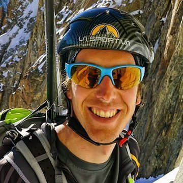 Person wearing a helmet and sunglasses with a mountainous background