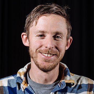 Man with a beard wearing a plaid shirt against a black background