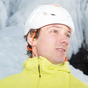 Person wearing a white helmet and yellow jacket in front of a snowy background