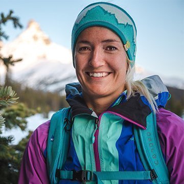 Person wearing a colorful jacket and helmet with mountains in the background
