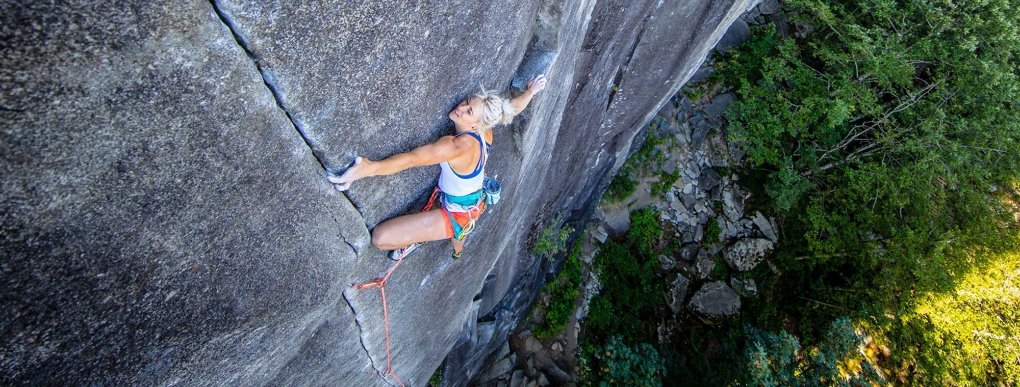 Person rock climbing on a steep cliff with greenery in the background