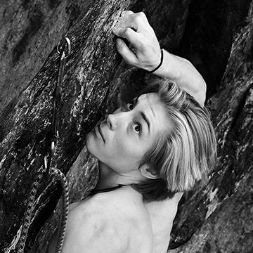 Person climbing a rocky wall with a focus on hand and face.