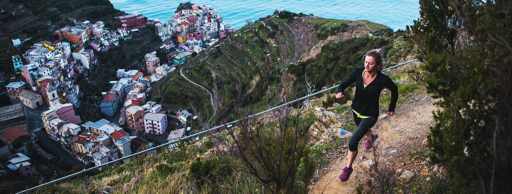 Person running on a trail with a scenic view of a coastal town in the background