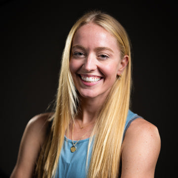 Woman with long blonde hair wearing a blue top against a black background