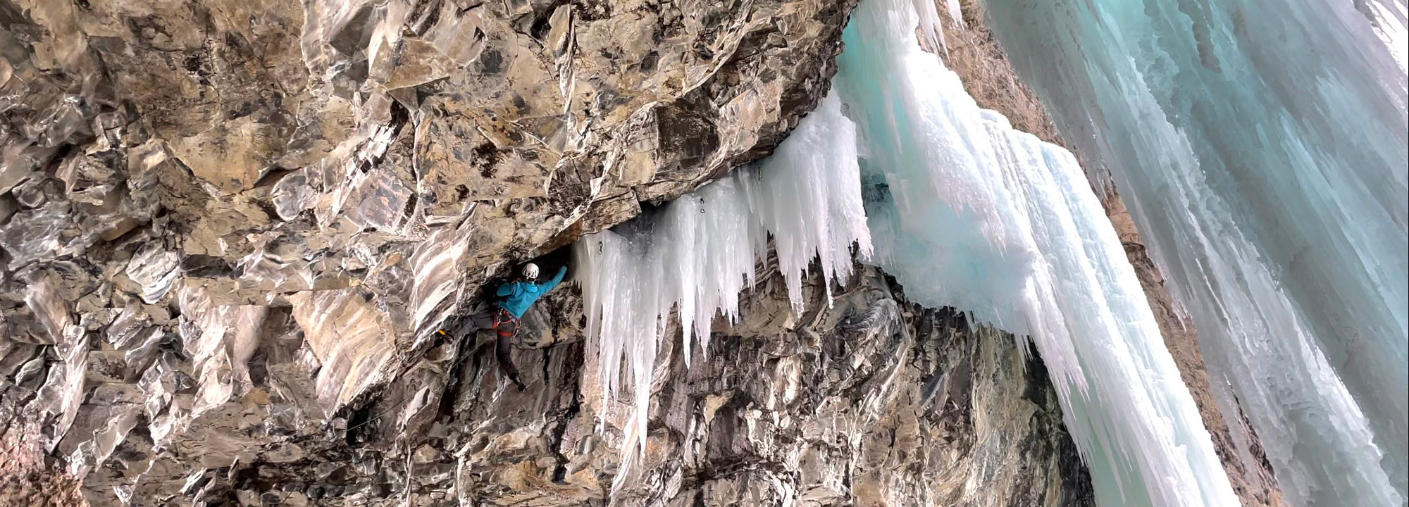 Person ice climbing on a frozen waterfall with rocky cliff face
