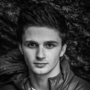 Black and white portrait of a person wearing a jacket against a textured wall.
