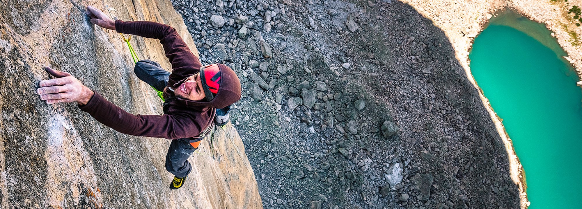 Person climbing a rocky cliff with a scenic view of a pool of water below.