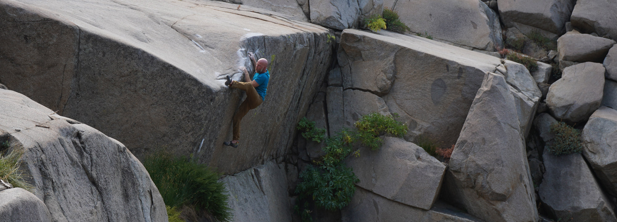 Person climbing a large rock formation with greenery.