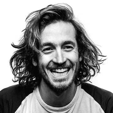 Black and white portrait of a man with long hair and a beard, wearing a dark shirt and light-colored sweater.
