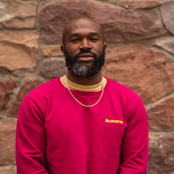 Man wearing a red sweatshirt with yellow text against a stone wall background