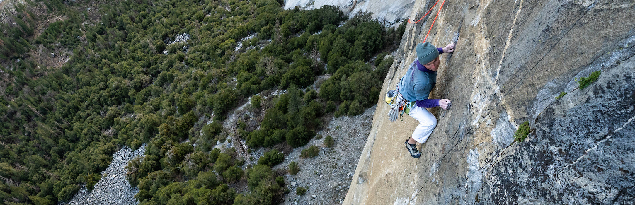Person rock climbing on a steep cliff with greenery in the background