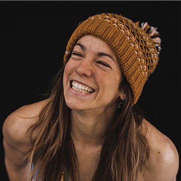 Woman wearing a mustard yellow knit beanie with pom-poms against a black background