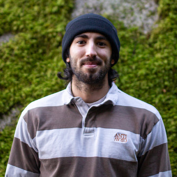 Man wearing a striped shirt and beanie standing against a green mossy wall