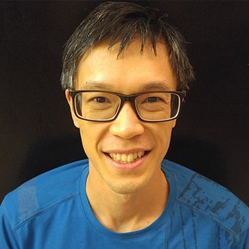 Person wearing glasses and a blue shirt against a dark background