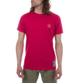 A person with long hair wears the La Sportiva Climbing On The Moon T-Shirt Men's (2025) in bright pink, featuring a small yellow logo on the left chest and blue patch near the hem, paired with olive green pants against a plain white background.