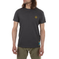 A person with long brown hair wears a La Sportiva Climbing On The Moon T-Shirt Men's (2025) in dark gray organic cotton with a small yellow logo on the left chest and khaki pants, standing against a white background for a retro vibe.