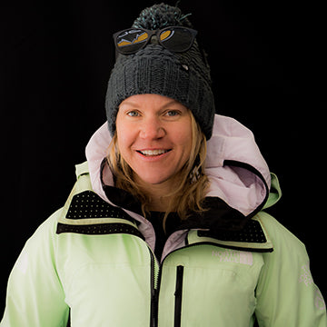 Person wearing a light green jacket with a hood and a black beanie on a black background