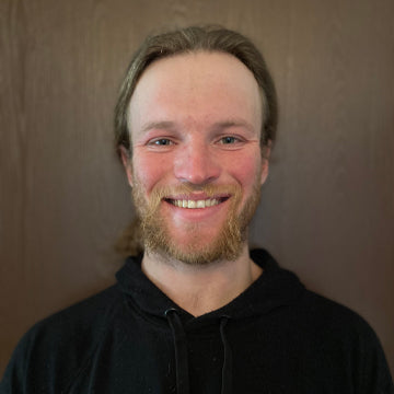 Man with a beard wearing a black hoodie against a plain background