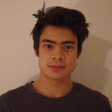 Person with dark hair and a neutral expression against a plain background