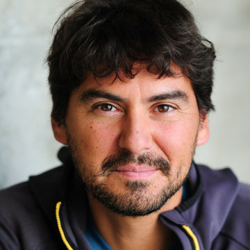 Man with dark hair and beard wearing a dark jacket with yellow accents.