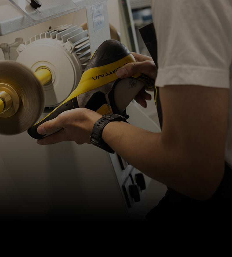 An employee works on re-soling a climbing shoe using a grinder tool.