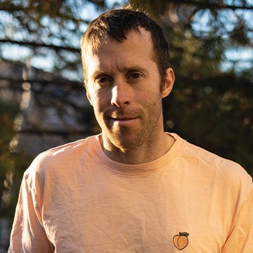 Man wearing a light pink t-shirt with a logo outdoors