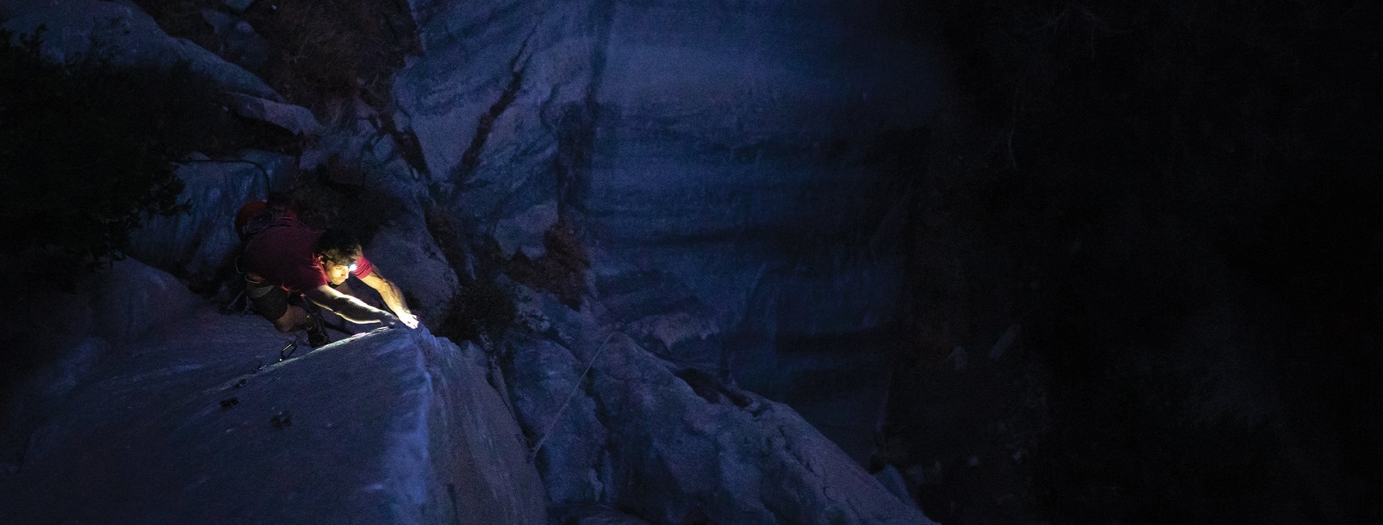 Person climbing a steep, snow-covered mountain face at night with a headlamp.