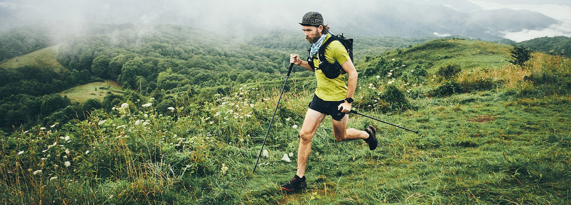Man running on a trail in a mountainous landscape with misty background