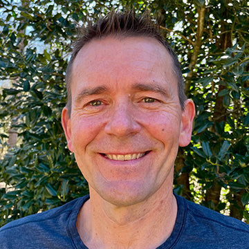 Man with a blue shirt standing in front of green foliage