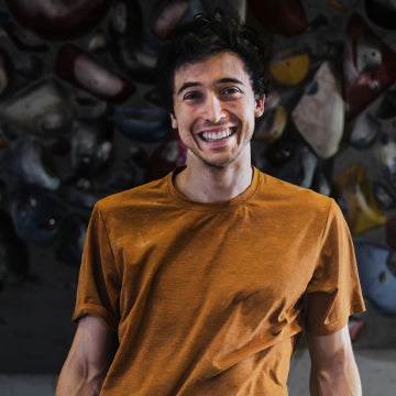 Man in an orange shirt standing in front of a rock climbing wall.