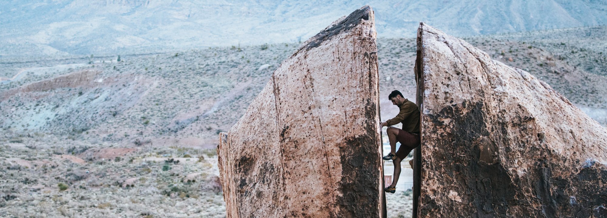 Person climbing between two large rock formations in a desert landscape