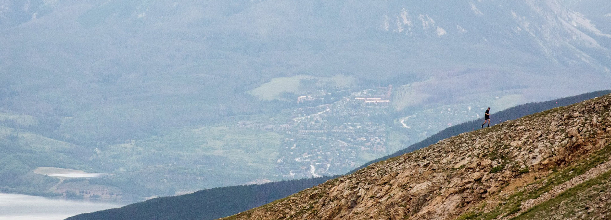 Person standing on a mountain with a scenic view of valleys and mountains in the background