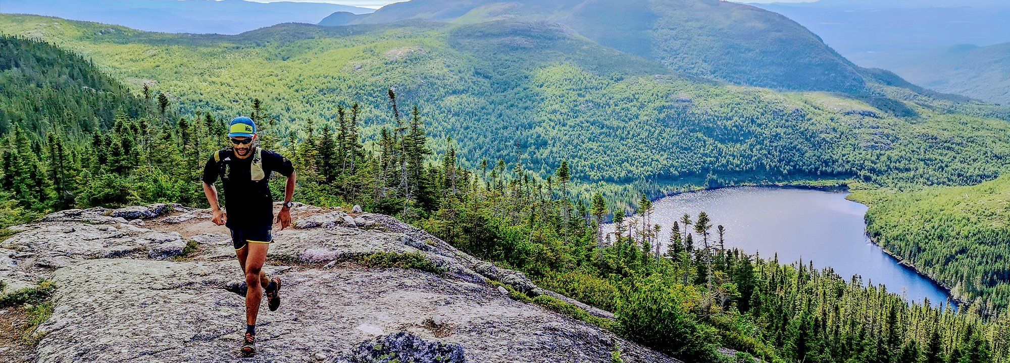 Person running on a mountain trail with a scenic view of a lake and mountains.