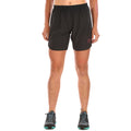 Une personne se tient debout, de face, vêtue d'un short de course La Sportiva Zen Shorts Women's - un short de course léger, sans frottement, avec un petit logo circulaire sur la jambe gauche - et de chaussures de course noires avec des semelles sarcelles. Le haut du corps n'est pas visible.