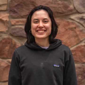 Person wearing a black hoodie with a visible brand logo against a stone wall.