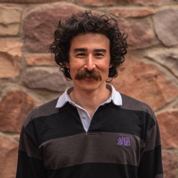 Man with a mustache wearing a striped shirt in front of a stone wall