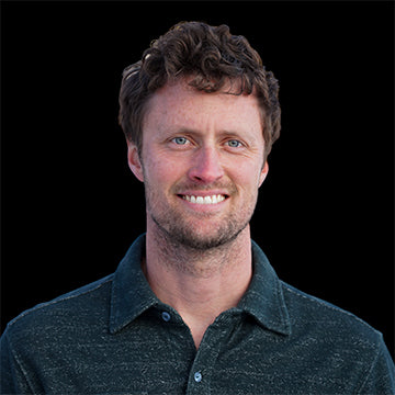 Man with a beard and short hair wearing a dark shirt on a black background