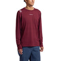 A person wears the La Sportiva Tour Long Sleeve Men’s (2025) maroon athletic shirt, featuring the brand logo on the chest, paired with blue pants and standing against a plain white background. This eco-friendly baselayer is ideal for active winter pursuits, providing comfort and style for outdoor enthusiasts.