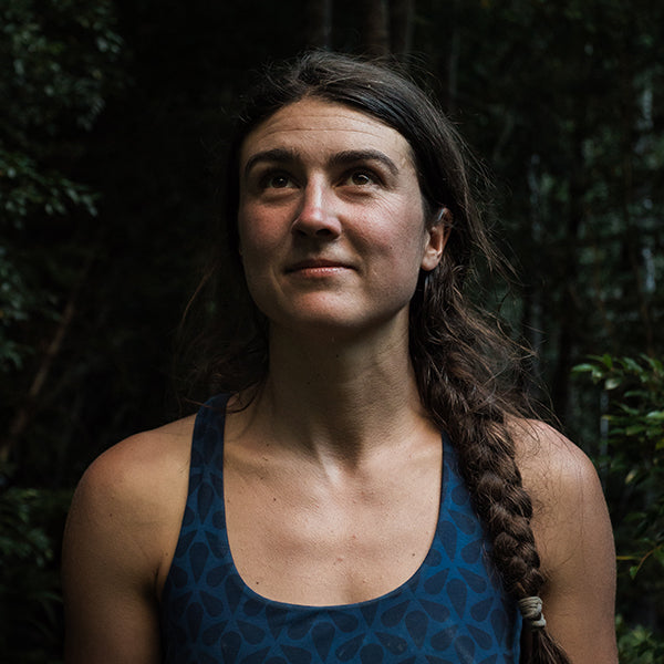 Woman with a braid standing against a dark, leafy background