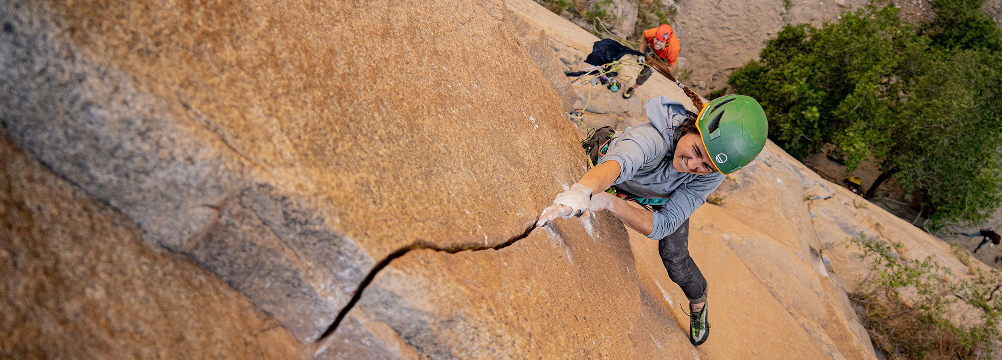 Person rock climbing on a steep, rocky cliff with green helmet and climbing gear.