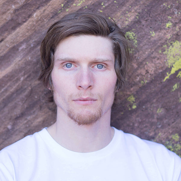 Man with a beard and blue eyes wearing a white shirt against a textured brown and green background