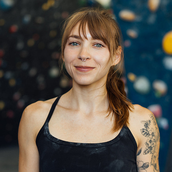 Woman with tattoos and piercings standing in front of a colorful wall.